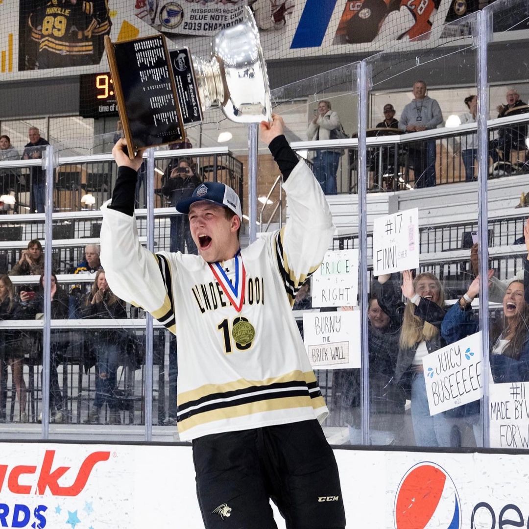 Leader playing hockey for Lindenwood University is celebrating a national championship holding a trophy over his head with a gold medal.
