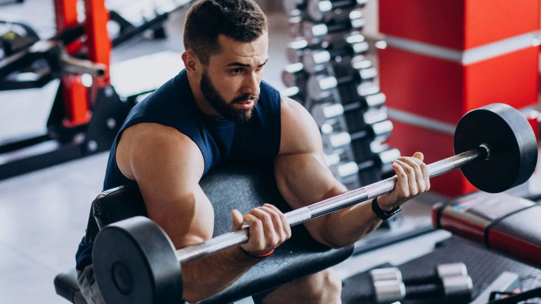 Man in a navy blue tank top performing a preacher curl with a straight bar