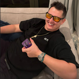 male smiling holding locked in sleep supplement in hand with sleep glasses on